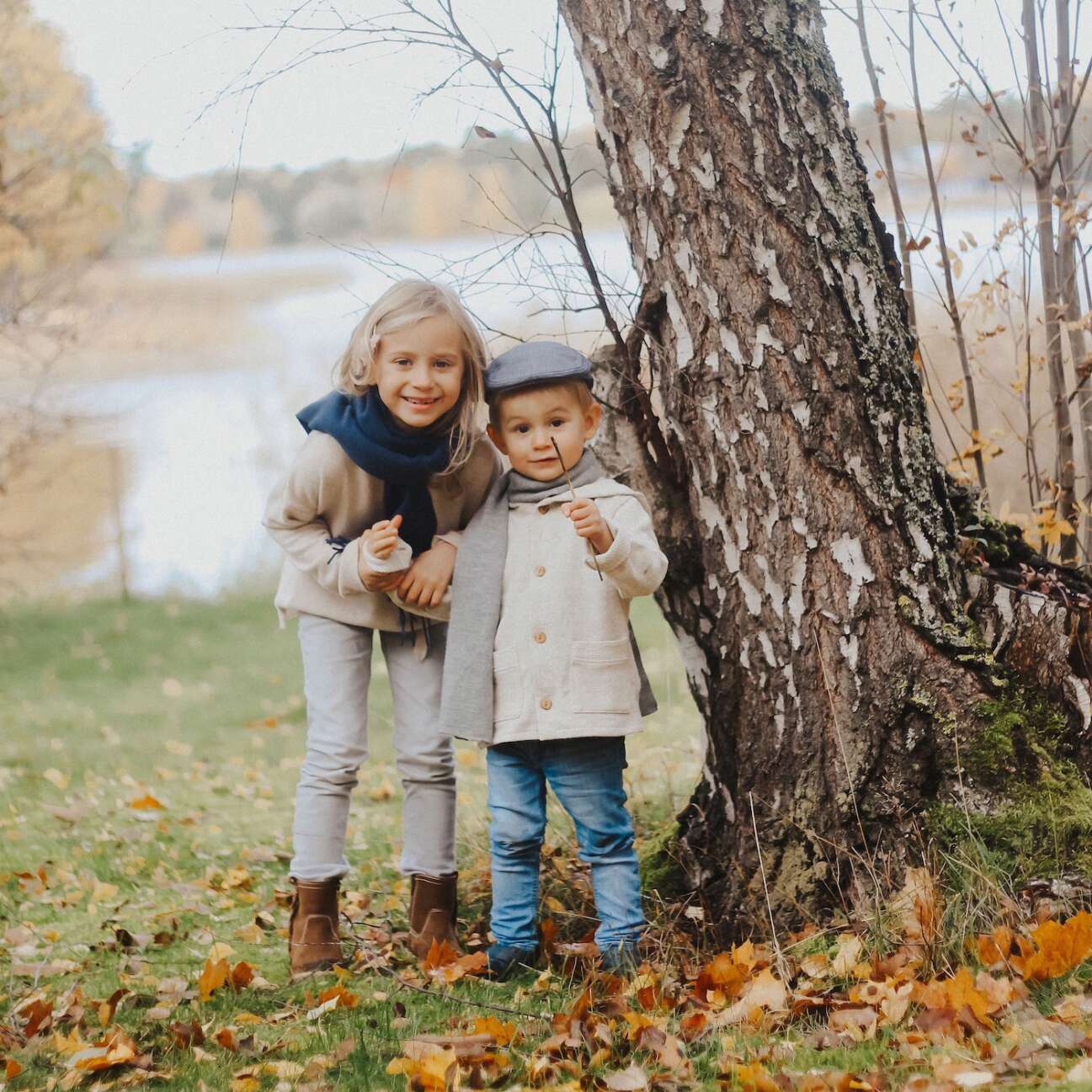 Two children photographed in an autumn scene standing next to a birch.